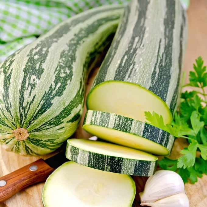Fresh striped summer squash zucchini sliced with garlic and parsley on a wooden cutting board