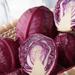 Red Acre seeds cabbage with deep red, globe-shaped heads, shown whole and halved in a basket.